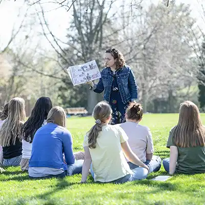Professor teaching class outdoors in a grassy shaded setting.