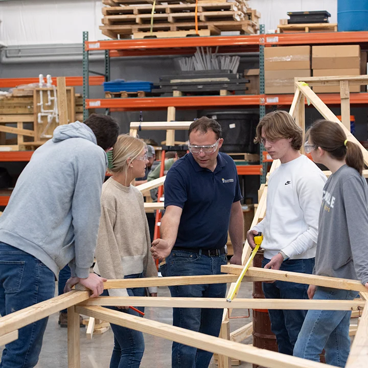 Professor instructing mechanical engineering students building a wooden structure.