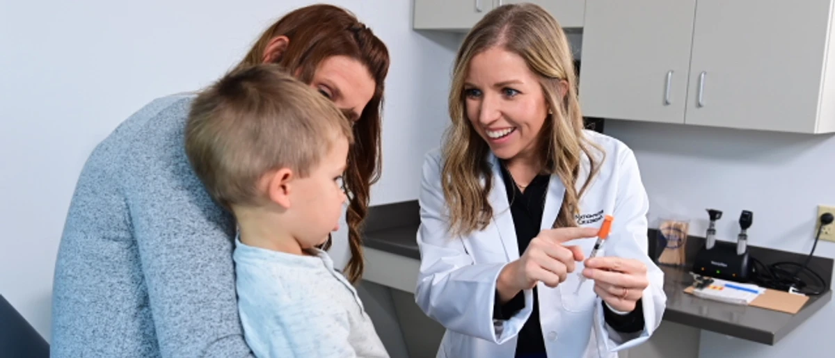 Cedarville University pharmacy student treating young child sitting on mother's lap in clinic setting