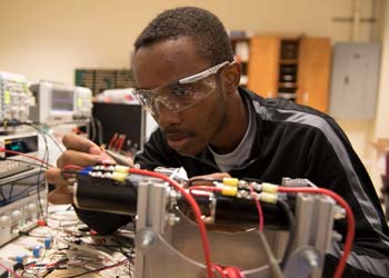 A man works on some electrical components in a room filled with electronics testing equipment