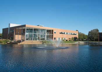 A building with large windows sits along a picturesque lake with a fountain