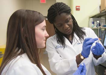 A professor and a student examine a vial in a pharmacy lab