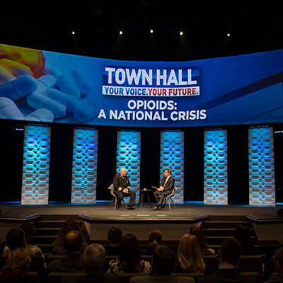 Town Hall event on stage, two men seated discussing Pharmacy related issues.