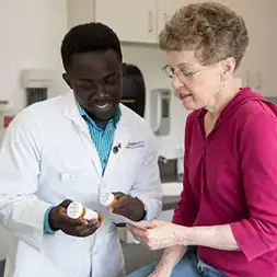 male Pharmacy student handing prescription bottles to elderly female patient in a clinic setting