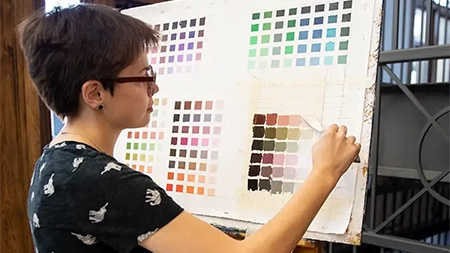 Female student paining a grid of color swatches.