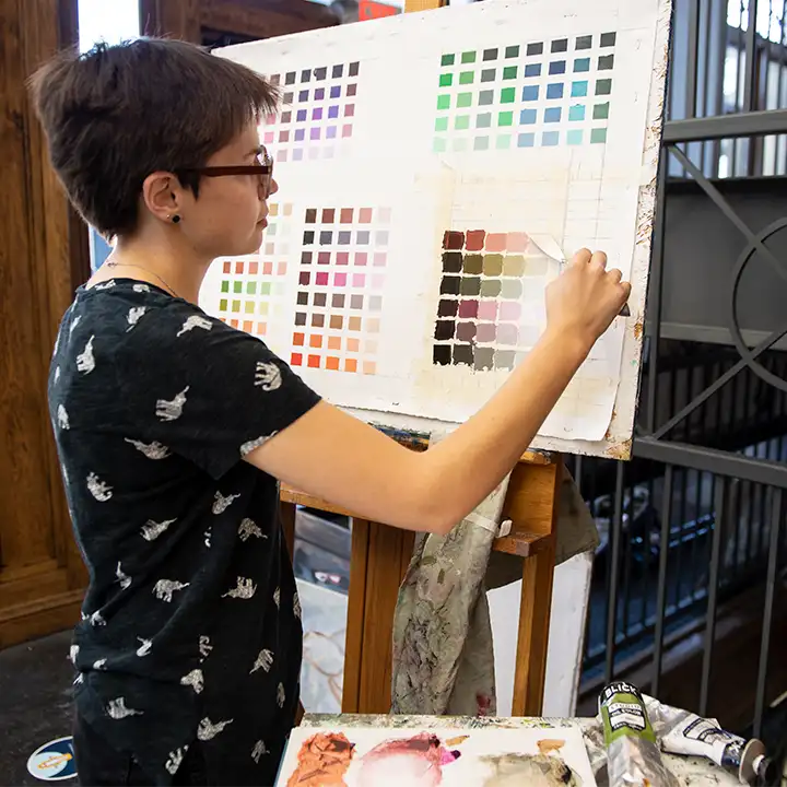 Female student paining a grid of color swatches.