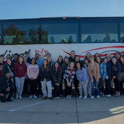 Students posing in front of a tour bus