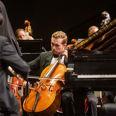 Student playing cello onstage with orchestra