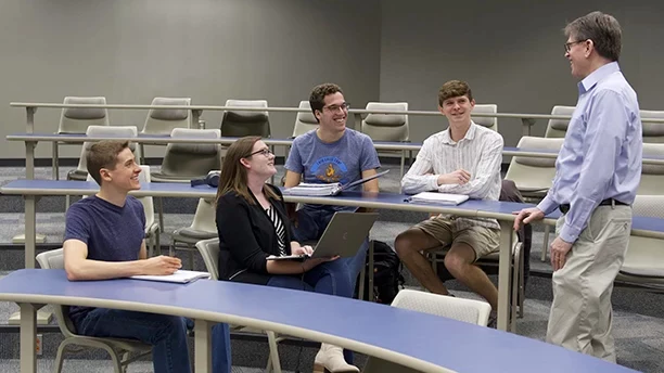 Students talking with a professor in a classroom.
