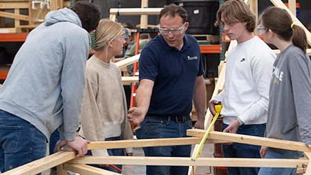 Professor instructing students in a engineering lab building a wooden structure.