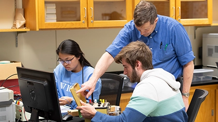 Professor working with students in an electronics lab.