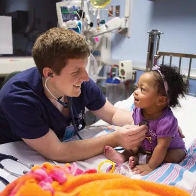 Male nursing student using a stethoscope to care for a toddler child.
