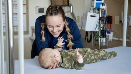 Nursing student caring for an infant on a examination table.
