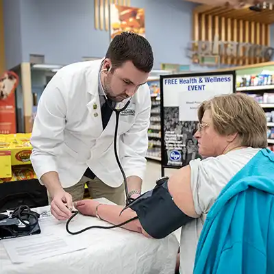 Pharmacist using a blood pressure cuff and stethoscope to care for a patient.