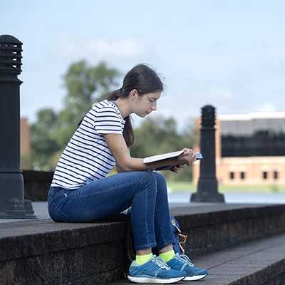 Female reading outdoors on steps by the lake.