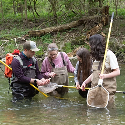 Professor and students wearing waders performing science experiments waist deep in a river.