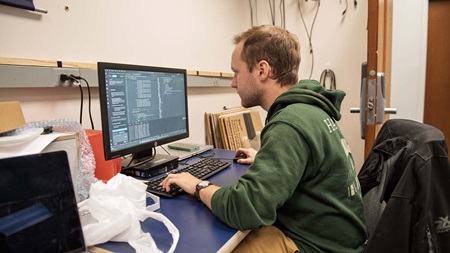 Computer science student sitting at a desktop computer with code open.