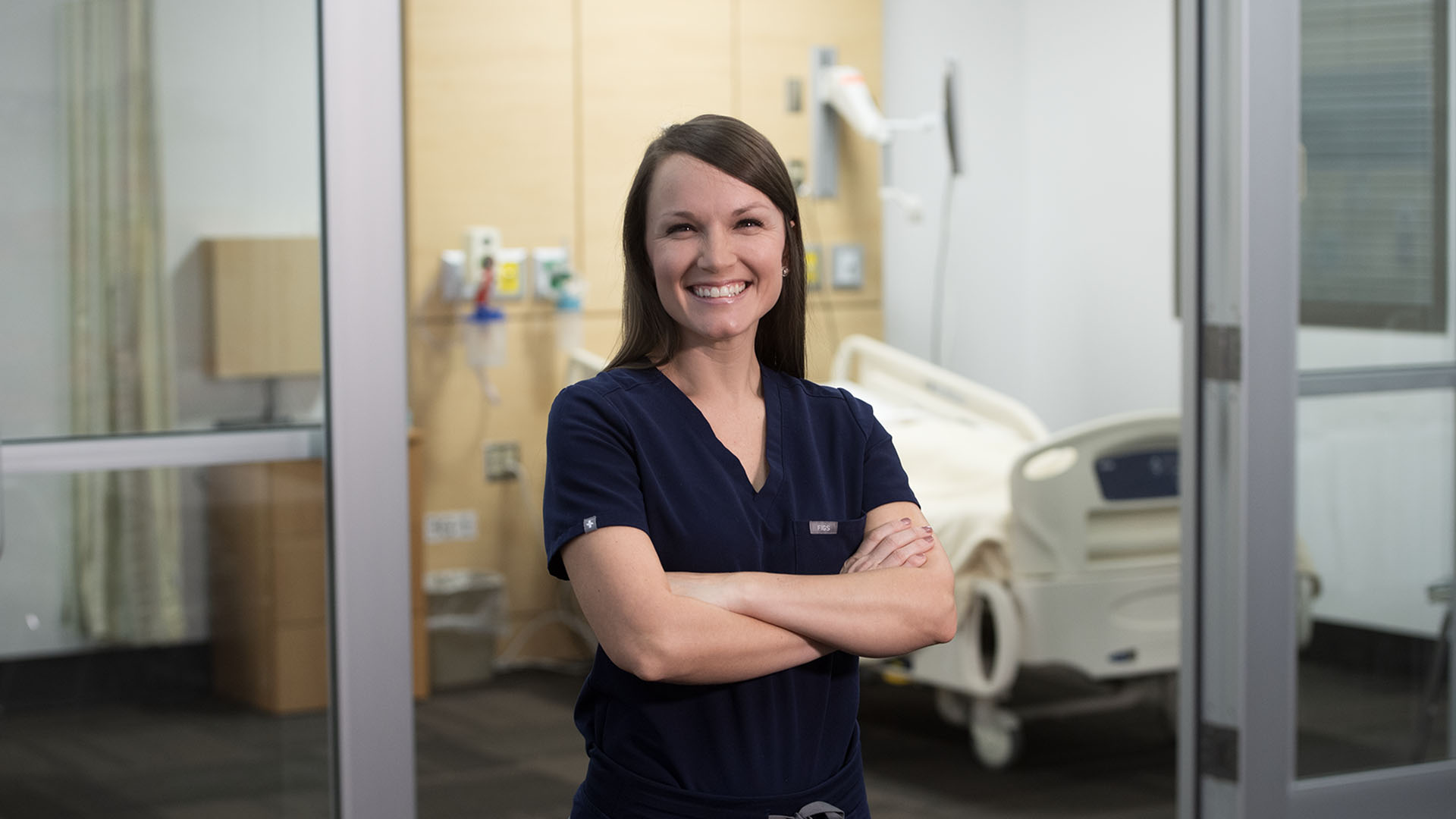 female advanced nursing practice student smiling in front of empty hospital simulation room