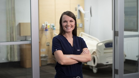 female advanced nursing practice student smiling in front of empty hospital simulation room