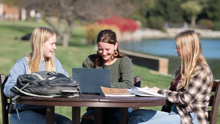 Three female college students studying at table outside