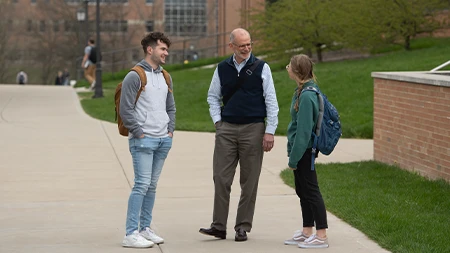 Professor talking with a male and female student on sidewalk outside