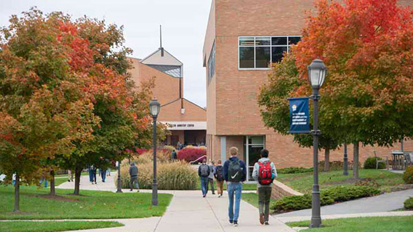Students walking on university campus amid trees at the peak of fall foliage.