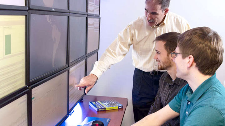 Professor teaching students at wall of computer monitors.