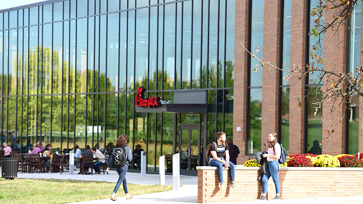 Students eating and talking outside a glass and brick building.