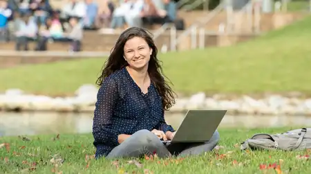 Woman sitting with laptop on grass near lake