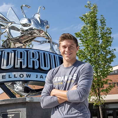 Student in a long-sleeve Cedarville University shirt standing in front of the Stinger Yellow Jacket statue on campus.