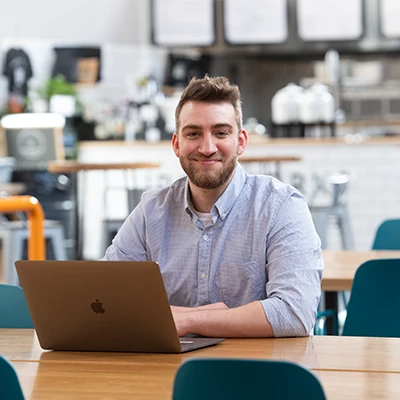Male student smiling at laptop in a modern campus cafe study space