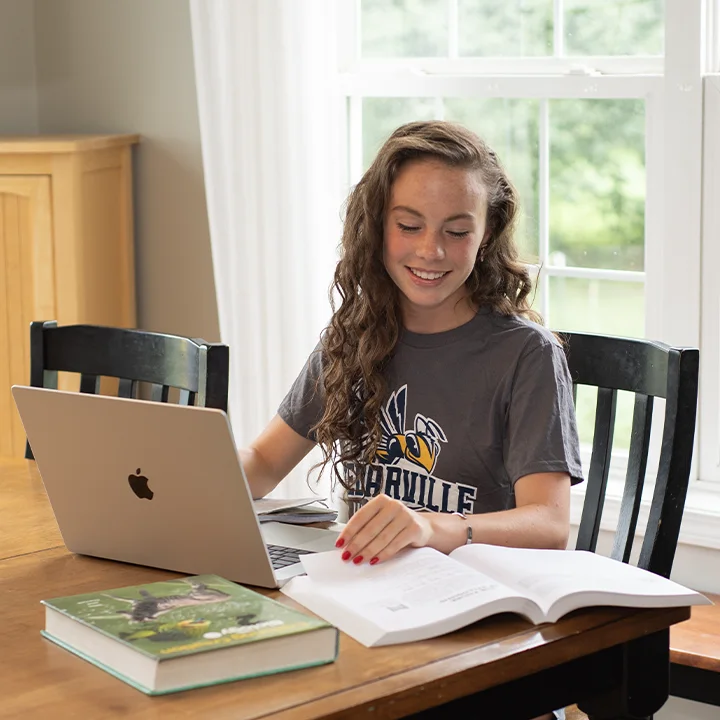 High school student studying with laptop and books at kitchen table
