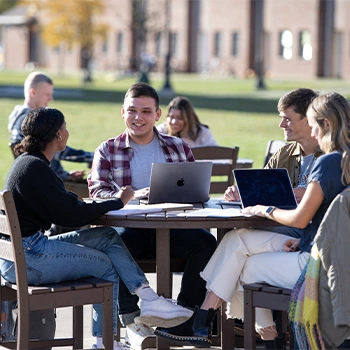 College students sitting around table outside laughing and studying