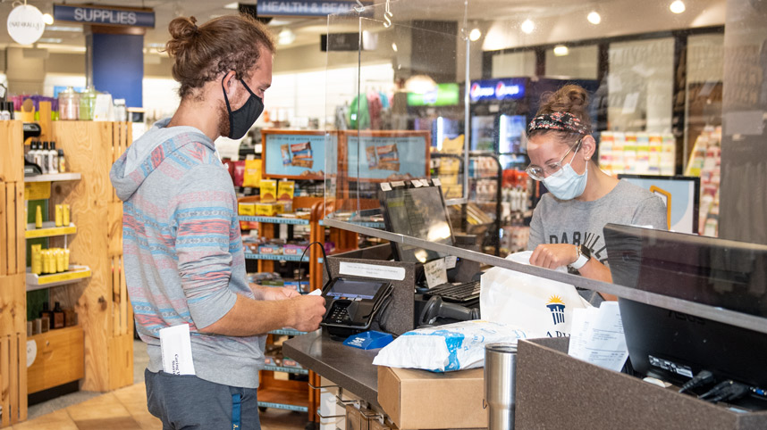 Student buying items in the bookstore with acrylic shield at the cash register