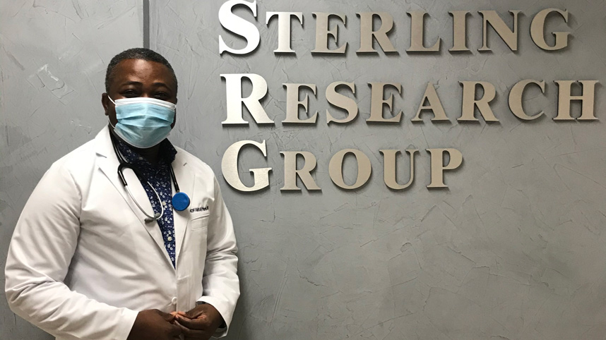 Dr. Kofi Amoah standing in front of Sterling Research Group sign