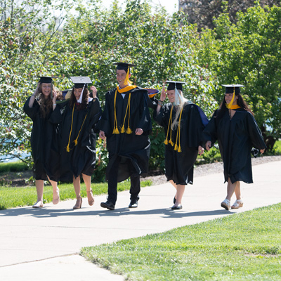 Five graduates walking past Cedar Lake