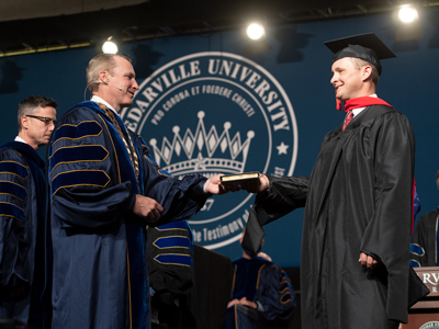 Dr. White conferring a degree on a graduate student with Dr. Mach looking on
