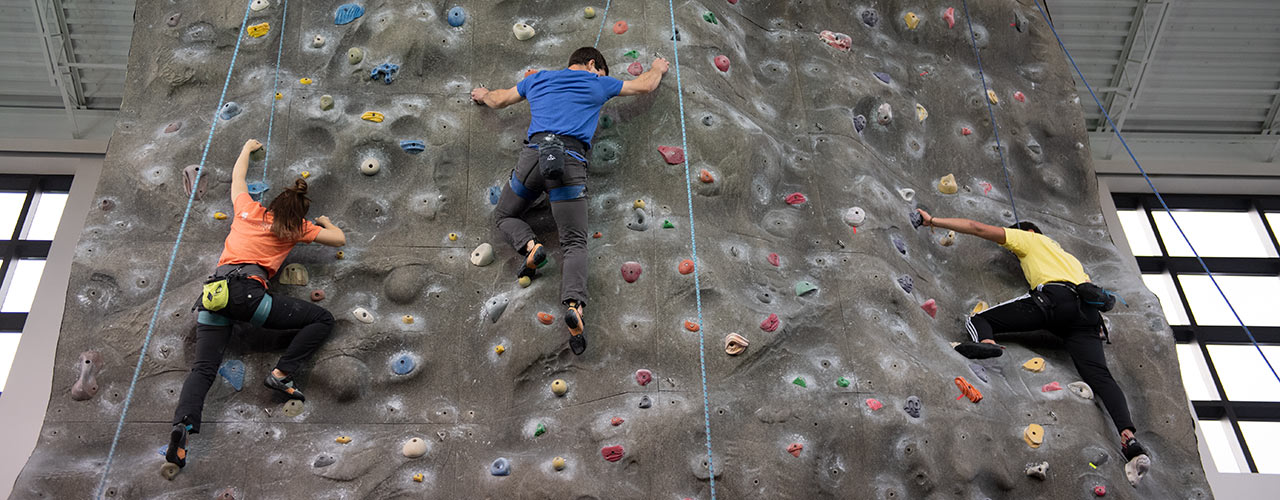 Three students ascending the climbing wall in the Fitness Center