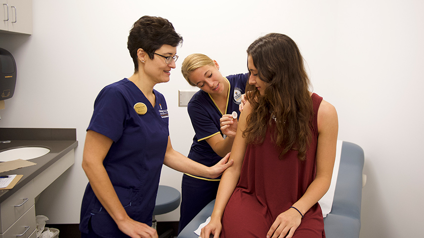 A nursing faculty supervises a nursing student administering a flu vaccine shot