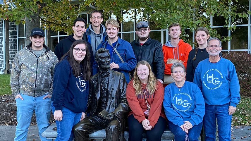 Dr. Kevin Sims, his nine students and his wife pose next to a statue of Lincoln in Gettysburg, Pennsylvania