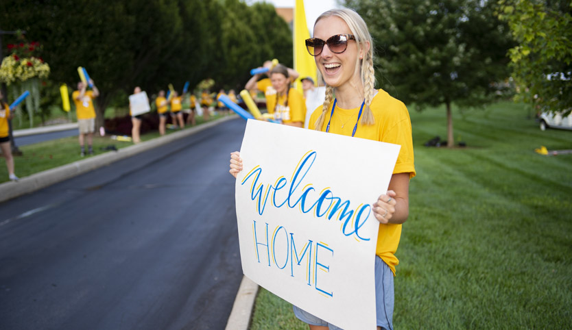 Girl holding welcome home sign to welcome freshman to campus