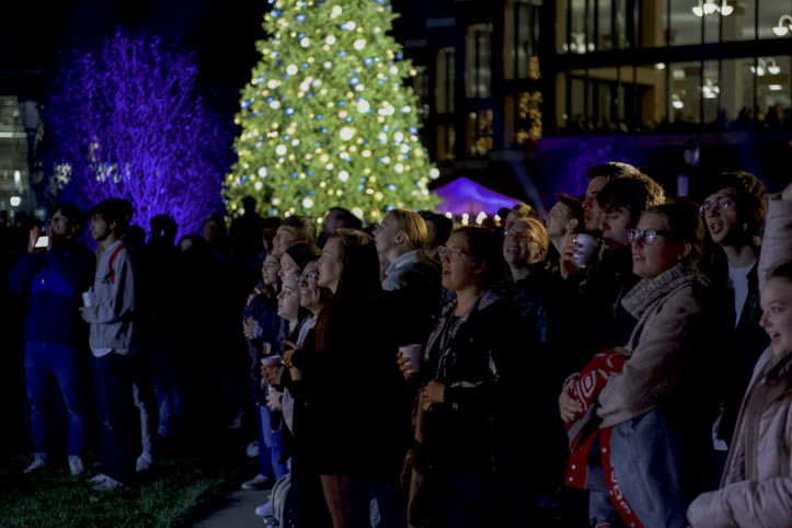 People around the lit Christmas tree singing Christmas carols
