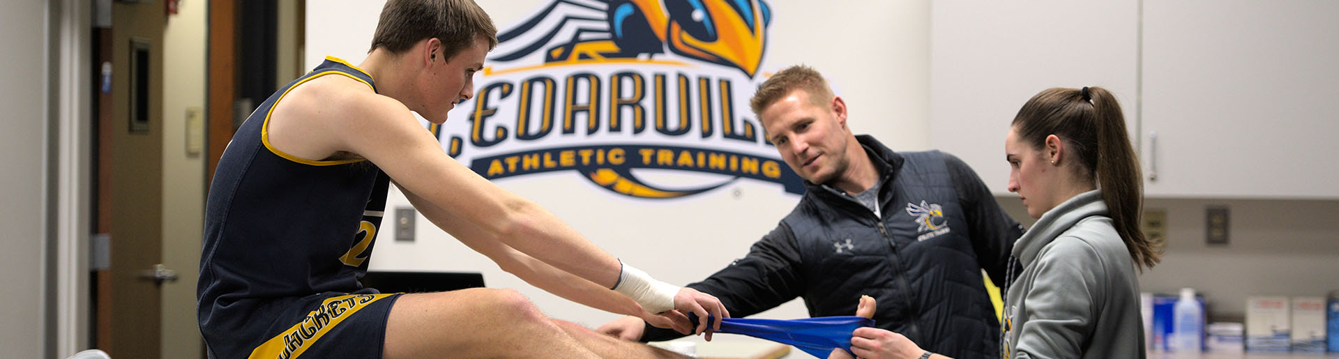 Cedarville University athletic trainer Wes Stephens and a student trainer help a basketball player in the training room.