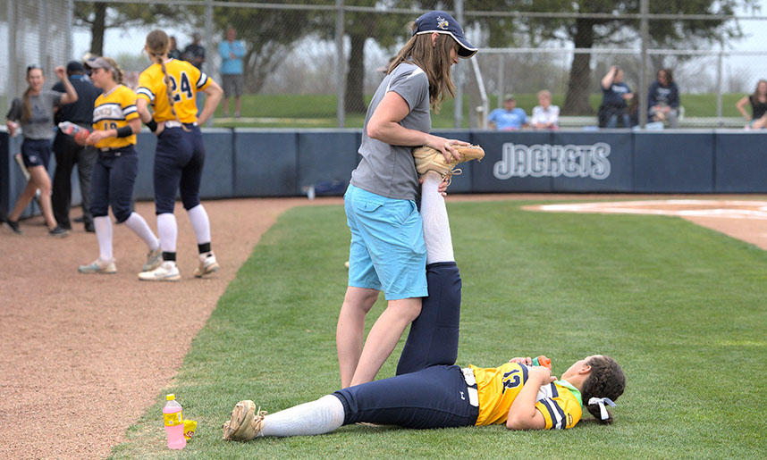 Prior to a softball game at Cedarville University, an athletic trainer helps a player stretch on the field.