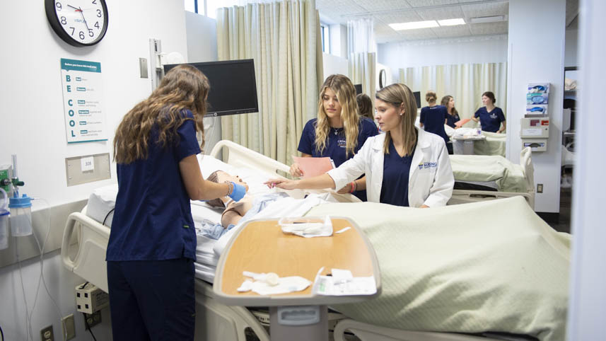 Clinical instructor guides female nursing students during clinical simulation.