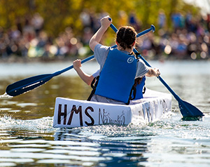 Engineering students paddle their cardboard canoe across Cedar Lake.