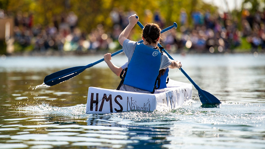 Engineering students paddle their cardboard canoe across Cedar Lake.