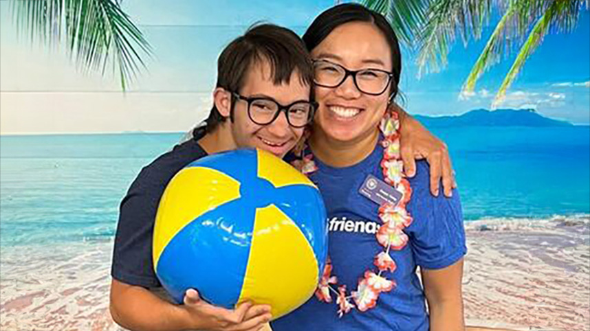 A Joni and Friends volunteer poses with a young man for a picture in front of a beach scene.