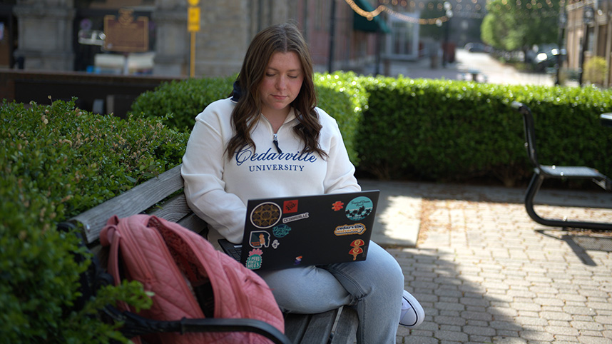 Abby Antram sitting on a bench working on a laptop.