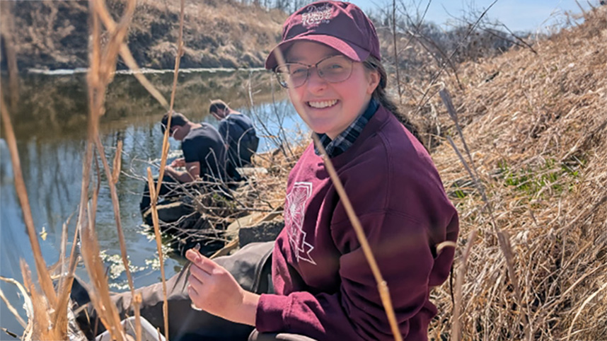 Abby Paulding sits beside a river collecting midges from the water.